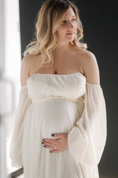 Beautiful portrait of pregnant woman in white dress. Concept of perfect pregnancy. Woman put her hand on belly. Future mother is waiting for baby — Stock Photo, Image