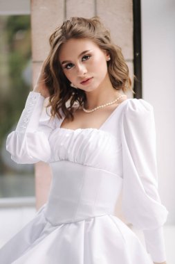 Zarif gelin pencere pervazında oturuyor ve elini saçına koyuyor. Beyaz elbiseli kadın pencereye bakıyor. Gelin sabahı konsepti