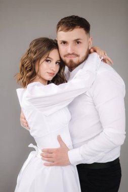 Sevgili geliniyle damadı kucaklaşın ve kameraya gülümseyin. Gri duvarın önündeki mutlu evlilik çifti. Stuio fotoekonomik durgunluk