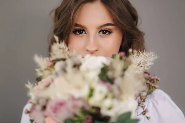 Portrait of young bride with wedding bouquet in front of grey backgound. Studio photophoot — Stockfoto