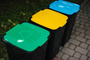Parktaki açık havada farklı renkte çöp kutuları geri dönüşüm yapıyor. Ağaç kapalı plastik kutular. Yeşil, evet ve mavi