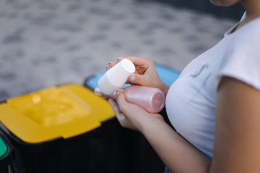 Geri dönüşüm kutusuna atılan kadın yıkanmış ve boş şampuan ve deodorant şişeleri. Kadın geri dönüşüm kutusundaki çöpleri atmak için paketleri inceliyor. İnsan elinin çöpü tuttuğu yakın plan.