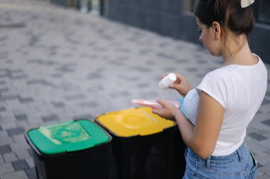 Geri dönüşüm kutusuna atılan kadın yıkanmış ve boş şampuan ve deodorant şişeleri. Kadın hangi geri dönüşüm kutusunda çöp atıldığını öğrenmek için paketlere bakıyor.