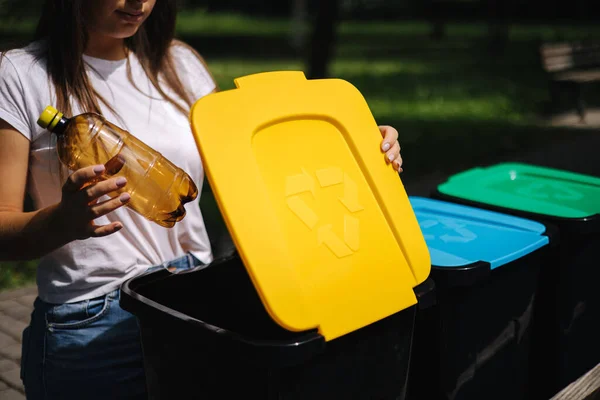 Ritratto donna gettando bottiglia d'acqua vuota di plastica nel cestino del riciclaggio. Cestini per il riciclaggio degli alberi all'aperto — Foto Stock