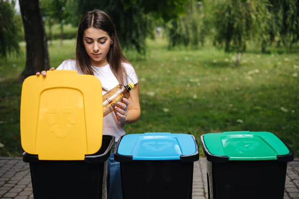 Portre kadın geri dönüşüm kutusuna boş plastik su şişesi atıyor. Ağaç geri dönüşüm kutuları açık havada — Stok fotoğraf