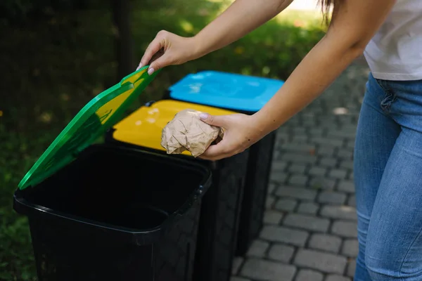 Primo piano ritratto donna mano gettando sacchetto di carta spiegazzata nel cestino del riciclaggio. Pattumiere per riciclaggio all'aperto colori diversi — Foto Stock