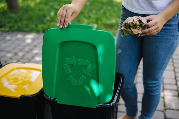 Primo piano ritratto donna mano gettando sacchetto di carta spiegazzata nel cestino del riciclaggio. Pattumiere per riciclaggio all'aperto colori diversi — Foto Stock