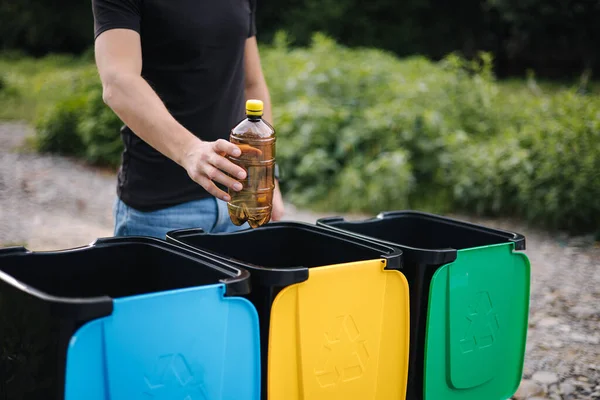 Primo piano della mano umana che getta una bottiglia d'acqua vuota nel cestino del riciclaggio. Cestini per il riciclaggio degli alberi all'aperto — Foto Stock