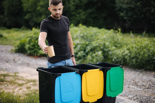 Ritratto di uomo che getta una tazza di cartone vuota dal cappuccino nel cestino del riciclaggio. Cestini per il riciclaggio degli alberi all'aperto — Foto Stock