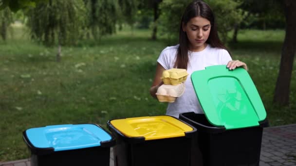 Las hembras sostienen basura, cartón de huevo y remolcan en la papelera de reciclaje. Primer plano de la mujer de pie por azul, yeallow y verde bin — Vídeos de Stock