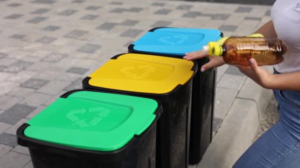 빈 플라스틱 물병 두 개를 재활용 쓰레기통에 던져 넣는 여성. 밖에 있는 나무 재활용 통 — 비디오