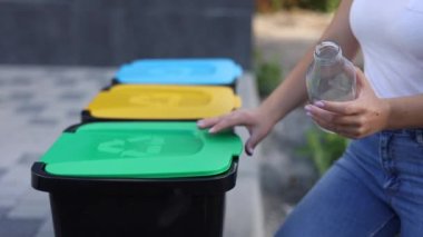 Kadınların el yapımı boş cam şişeyi geri dönüşüm kutusuna attıkları yakın plan. Parktaki plastik kutuların farklı renkleri