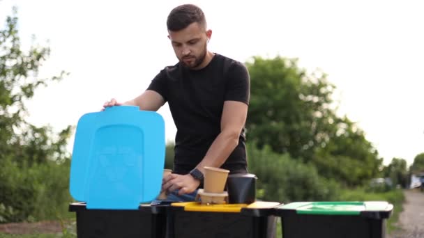 Een man die in de afvalbak gooit. Aantrekkelijke jonge man aparte plactic deksel met kartonnen beker en duw in verschillende bak — Stockvideo