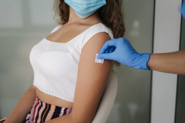 Tıbbi maske takan hastaya iğne yapmadan önce elinde şırınga tutan ve pamuk kullanan koruyucu eldivenli doktorların yakın çekimi. Covid-19 veya koronavirüs aşısı