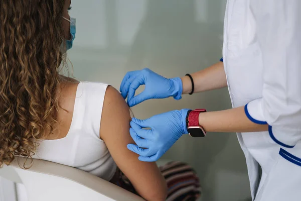 Female doctor in protective gloves put patchafter vaccination in shoulder. Covid 19 vaccination. Women getting injection in shoulder. Vaccine clinical trials concept, corona virus