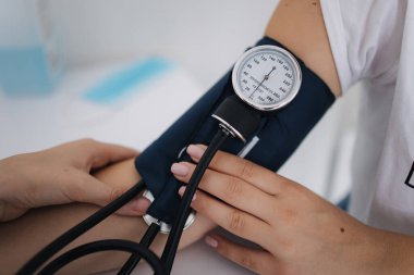 Doktorun steteskopla sphygmomanometre kullanarak kan basıncını ölçtüğü yakın plan.
