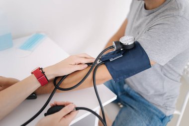 Yüksek tansiyonu olan genç bir adam. Steteskopla sphygmomanometre kullanan kadın doktor klinikteki bir hastanın tansiyonunu ölçüyor. Tıbbi muayene. Kapat.