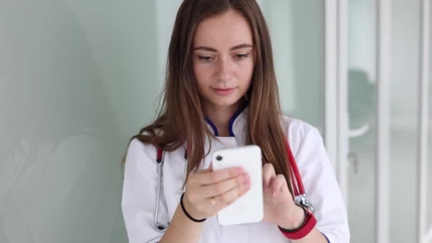 Youg médico femenino utilizando el teléfono durante la pausa en clicic — Vídeos de Stock