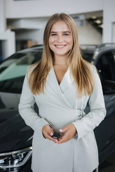 Portrét krásné a mladé podnikatelky v autosalonu. Žena držet klíče z jejího nového auta — Stock fotografie