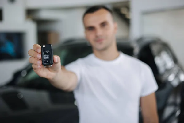 Porträtt av handosom man i bil showroom. Mannen håller nycklarna från hennes nya bil. Nycklar i fokus — Stockfoto