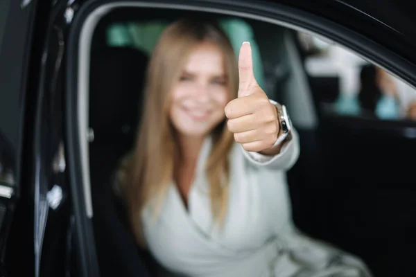 Atraktivní mladá obchodní žena sedí v autě v autosalonu. Žena vybírá nové auto. Krásná blond žena v obleku. Rozostřená žena — Stock fotografie