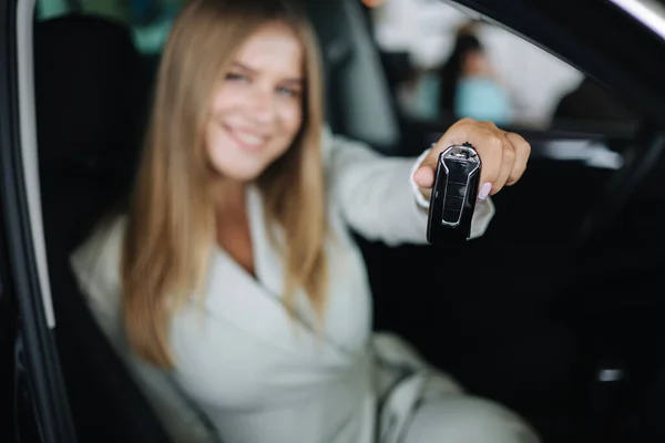 Atacado jovem bussines mulher sentada no carro no showroom do carro. Mulher escolhendo carro novo. Cabelo loiro bonita fêmea de terno segurar chaves. Chaves em foco — Fotografia de Stock