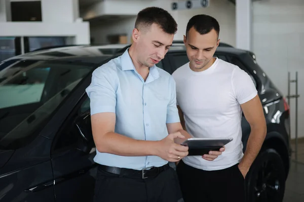 Försäljare som säljer bilar hos bilhandlare. Man väljer bil i bilens showroom — Stockfoto