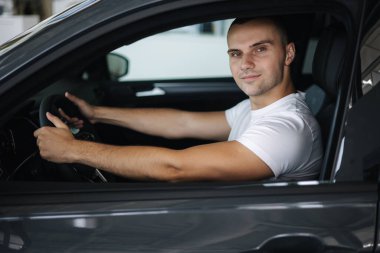 Araba galerisindeki yeni arabasında oturan adam. Arabadaki yakışıklı adamın portresi.