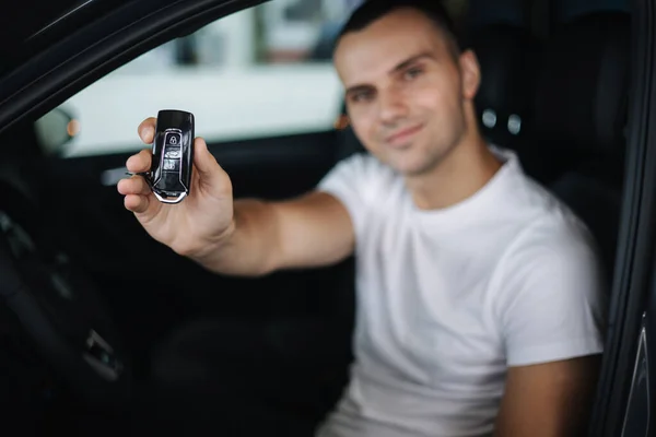 Mannen sitter i sin nya bil i bilens utställningsrum. Porträtt av stilig man i bilen håller nycklar i händerna. Nycklar i fokus — Stockfoto