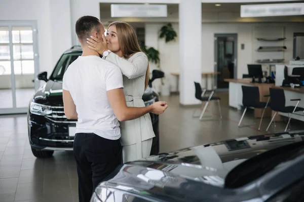 Glückliche Frau umarmt ihren Mann nach dem Autokauf im Autohaus. Mann und Frau kaufen neues Auto — Stockfoto