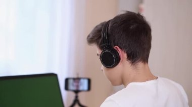 Genç çocuk odasında dizüstü bilgisayarında oyun oynuyor. Buharlı gemi kablosuz kulaklık kullanıyor. Mutlu oyuncular bütün gün oynar. Yan görünüm