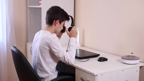 Хлопчик-підліток грає в гру на своєму комп'ютері в білій кімнаті. Gamer знімає відео на веб-камеру на ноутбуці та телефоні на штатив — стокове відео