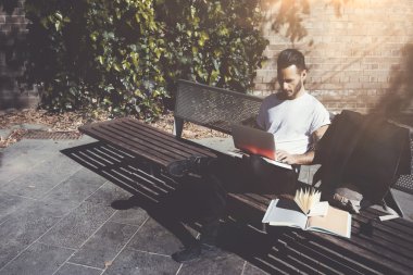 Fotoğraf adam şehir parkı bankve mesaj defteri mesajlaşma oturuyor. Kablosuz internet kullanımı. Üniversitede okumak, sınavlara hazırlanmak. Kitap, genel tasarım dizüstü bilgisayar kullanın. Yatay, yumuşak gölgeler
