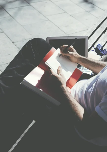 Zdjęcie mężczyzna siedzący city park i SMS-y wiadomość notatnika. Studiuje na Uniwersytecie, pracy projektu, kampusu. Za pomocą książki, ogólny projekt laptopa. Pionowe — Zdjęcie stockowe