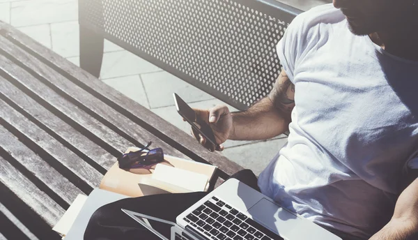 Foto man zittend stadspark Bank en SMS-bericht smartphone. Met behulp van draadloos internet. Studeren aan de Universiteit, voorbereiding voor examens. Gebruik boek, generieke design laptop. Horizontaal, close-up — Stockfoto