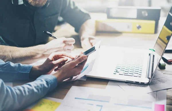 Incontro d'affari, collaborazione. Foto giovani uomini d'affari equipaggio che lavorano con nuovo progetto di startup in loft moderno. Generico smartphone di design che tiene le mani femminili, tavolo in legno per laptop. Effetto orizzontale, pellicola — Foto Stock