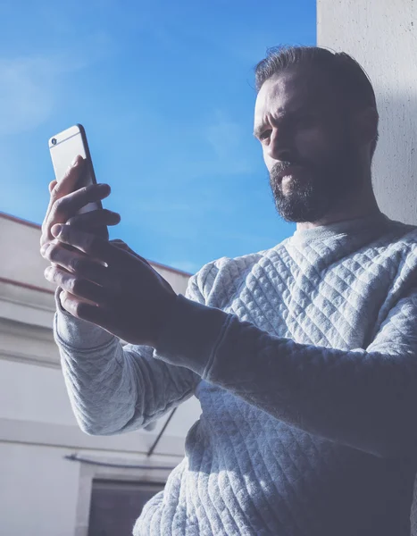 Foto bärtiger Mann macht Selfie-Handy. Mann mit zeitgenössischem Smartphone, blauer Himmel, sonniger Tag. vertikal, Filmeffekt — Stockfoto