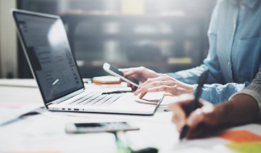 Pazarlama, ekip toplantısını analiz etti. Genç işadamları ekibi modern loft yeni başlangıç projesi ile çalışıyor. Ahşap masa üzerinde genel tasarım dizüstü bilgisayar. Akıllı telefon elleri. Yatay, film efekti, bulanık arka plan