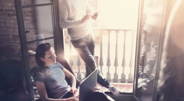 Genç çift birlikte çalışıyor. Fotoğrafçı kadın ve erkek modern çatı katında yeni bir proje üzerinde çalışıyorlar. Çağdaş defter ve akıllı telefon kullanarak. Yatay, film efekti. Bulanık arkaplan