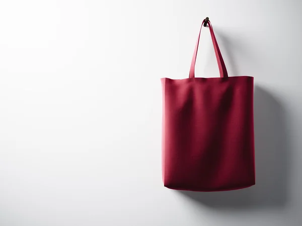 Bolso textil de algodón rojo foto colgando del lado derecho. Fondo de pared blanco vacío. Textura muy detallada, espacio para la publicidad. Horizontal. 3d renderizar — Foto de Stock