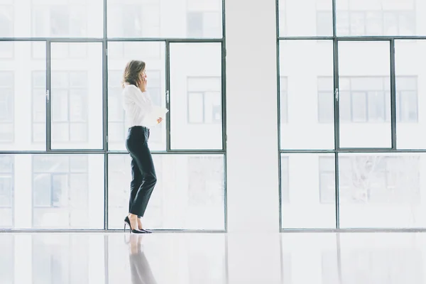 Foto affärskvinna bär moderna kostym, talar smartphone och håller papper i händerna. Öppet utrymme loft office. Panoramafönster bakgrund. Horisontella mockup. — Stockfoto