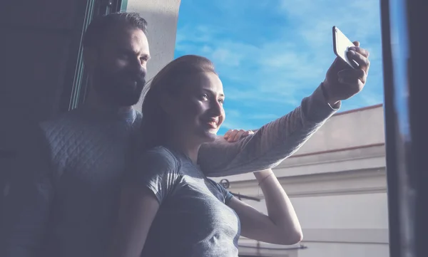 年轻夫妇一起过暑假.在现代阁楼里，拍照的女人和留着胡子的男人在自拍手机。使用当代智能手机。横向、电影效果. — 图库照片