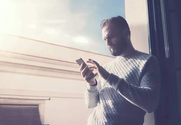 Hombre barbudo retrato en loft moderno. Hombre usando smartphone contemporáneo, fondo de cielo soleado. Horizontal, efecto de película —  Fotos de Stock