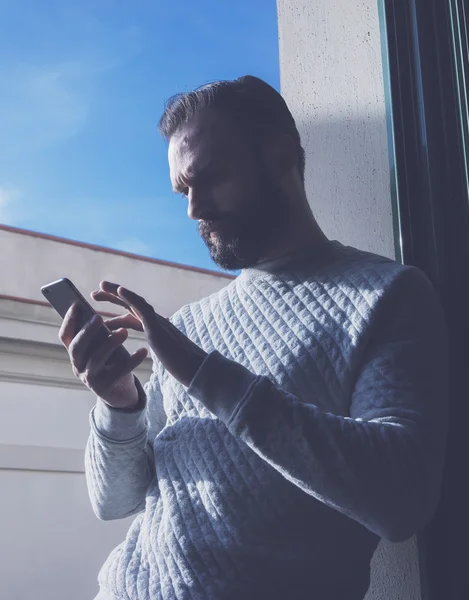 Portræt skægget mand rører skærmen mobiltelefon. Mand, der bruger moderne smartphone, blå himmel baggrund. Lodret, film effekt - Stock-foto