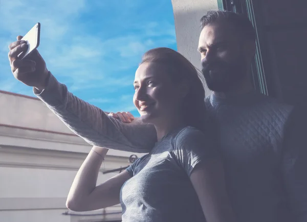Young couple summer holiday city. Photo woman and bearded man making selfie mobile phone in modern loft. Using contemporary smartphone, smiling. Horizontal, film effect. — Stockfoto