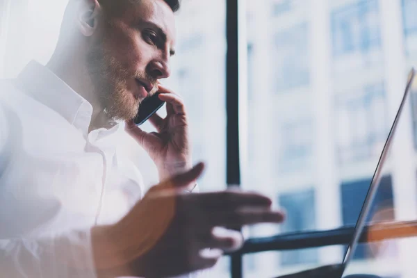 Photo bearded adult businessman working on modern loft office. Man wearing white shirt and talking smartphone. Panoramic windows background. Horizontal, film effect, bokeh — Stock Photo, Image