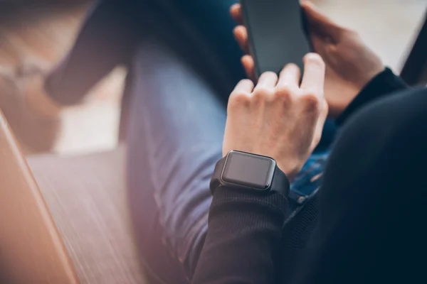 Closeup photo of female hands touching screen smartphone and wearing generic design smart watch. Film effects, blurred background. Horizontal