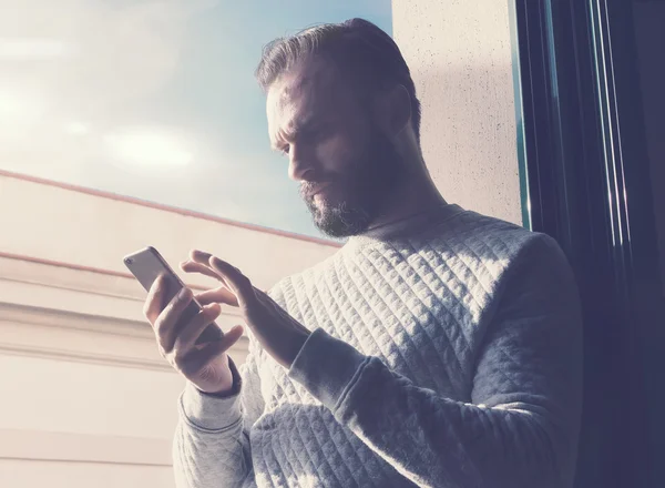 Retrato barbudo hombre tocando la pantalla del teléfono móvil. Hombre usando smartphone contemporáneo, fondo de cielo soleado. Horizontal, efecto de película — Foto de Stock
