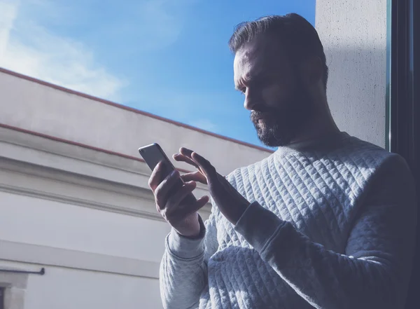수염 이 있는 사람 이 스크린 휴대 전화에 손을 대고 있다. 현대의 스마트폰을 사용하는 남자, 푸른 하늘 배경. Horizontal, film effect — 스톡 사진