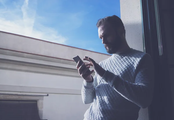 Porträt bärtiger Mann in modernem Loft. Mann mit zeitgenössischem Smartphone, blauem Himmelhintergrund. horizontal, Filmeffekt — Stockfoto